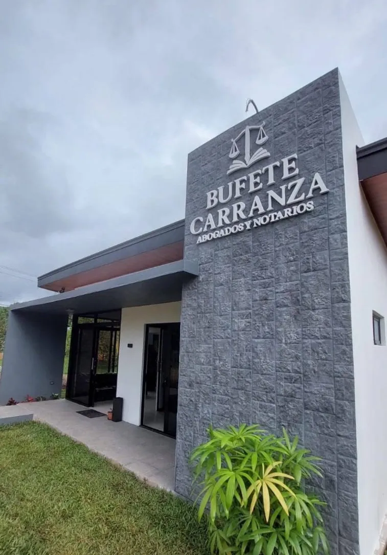 Fachada del Bufete Carranza: muro de piedra gris con el rótulo del bufete, paredes blancas y alero de madera.